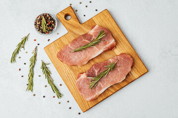 Freshly prepared pork chops with seasoning herbs on wooden cutting board