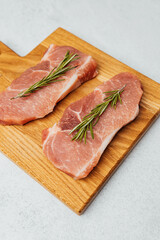 Fresh pork chops with rosemary on wooden cutting board at kitchen