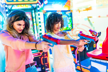 Two female friends playing arcade shooting game together