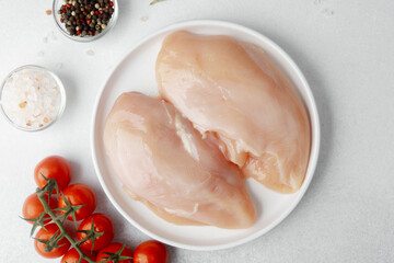 Closeup of raw chicken breasts on white plate with herbs and tomatoes