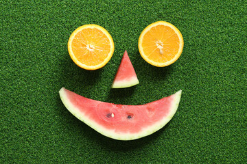 Fruit face. Orange halves and watermelon slice on green grass background, top view. Fruit abstract...