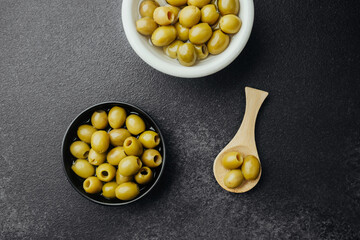 Green olives in ceramic bowls and wooden spoon on stone background