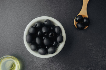 Black  olives in black bowl with  olive oil on a dark stone background