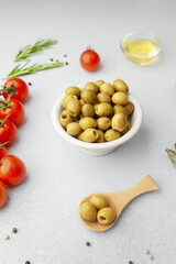 Green olives in ceramic bowl with tomatoes asparagus and seasonings on white table