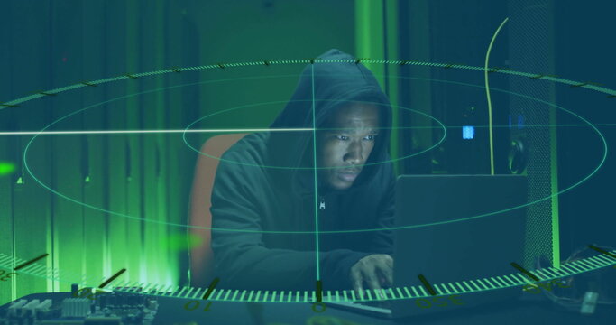 Monitoring hacker in hoodie scanning laptop and circuit board in data center, holographic overlay