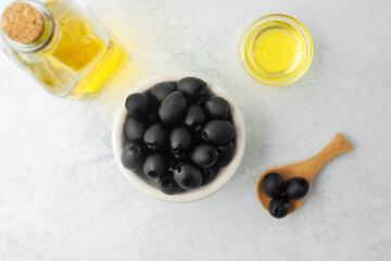 Black olives in bowl with bottle of olive oil on light background
