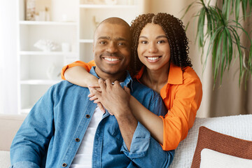 Closeup portrait of happy young Black couple posing at home, woman embracing man from behind on...