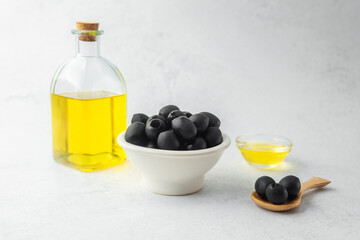 Black olives in bowl with bottle of olive oil on light background