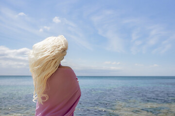 Blonde hair beach: Woman stands, enjoys summer breeze on sunny seaside, showing carefree vacation freedom.
