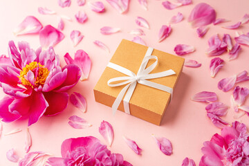 Gift box with white ribbon and pink peony flowers on pastel background with scattered petals
