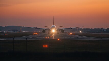 Fototapeta na wymiar A plane prepares for takeoff at sunset, illuminated by runway lights with a vibrant sky in the background.