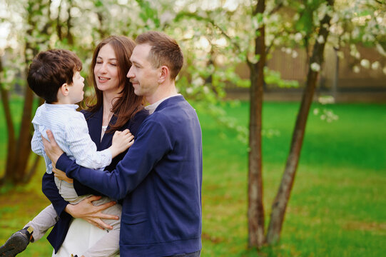 happy family bonding outdoors, parents embrace son in lush park setting, blossoms in background. casual attire underlines natural joy, perfect family lifestyle moment, spring vibes - Powered by Adobe