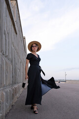 Confident woman in black dress stands beside modern wall