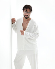 confident fashion guy with glasses in white costume leaning on a wall