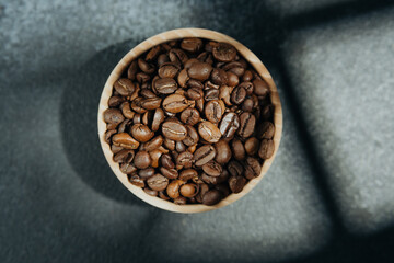 Coffee beans in wooden bowl with shadow on dark background