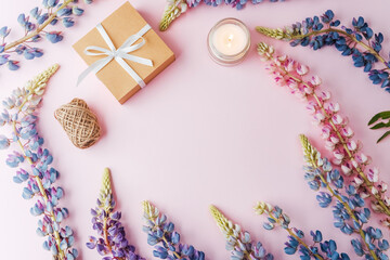 Gift box and blank card with lupin flowers and candle on pink background, copy space