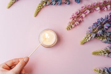 Hand lighting candle with lupine flowers on pink background