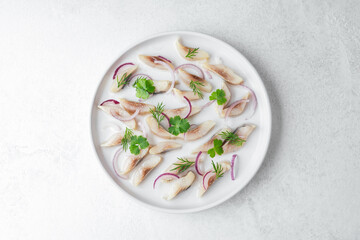 Marinated herring slices with red onion and herbs on white plate over light background