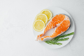 Closeup raw salmon steak with lemon slices and rosemary on plate over light background
