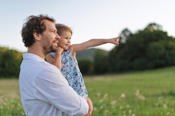 Father standing in the middle of meadow, holding small daughter in the arms.