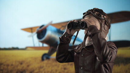 Child dressed as a historical pilot scans the sky with binoculars, standing in a sunny field with a vintage biplane blurred in the background.