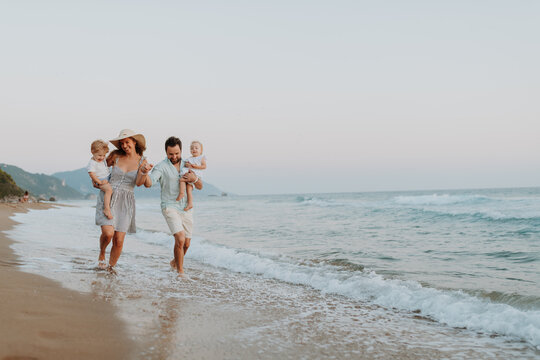 Fototapeta A family with two toddler children walking on beach on summer holiday at sunset.