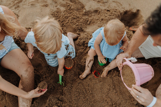 Two toddler children playing on sand beach with paretns during summer holiday.