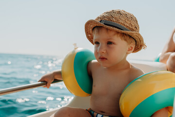 A small boy with arm floaties sitting on boat on summer holiday.