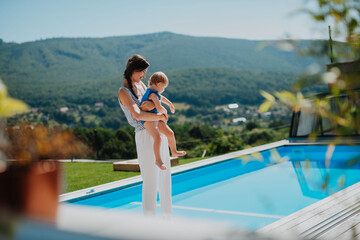Mom holding little daughter and showing her hotel pool.
