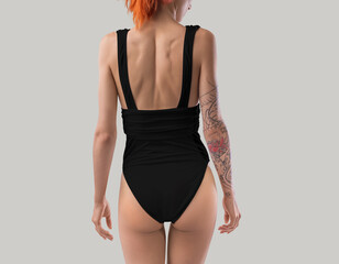Template of a black one-piece swimsuit, with a bare back, on a red-haired slim girl with a tattoo, isolated on the background.