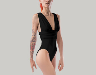 Mockup of a black one-piece monokini with a neckline on a red-haired girl with a tattoo, side view, isolated on the background.
