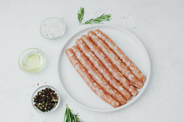 Uncooked sausages on white plate with rosemary and spices