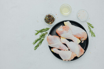 Raw chicken drumsticks on black plate with rosemary and spices
