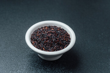 Black rice in white bowl on dark background with loose grains