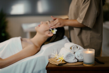 Spa essentials arranged on a wooden tray including rolled white towels, and aromatherapy candle