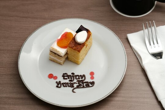 A plate with two types of cakes decorated with fruit, chocolate writing, and a warm message "Enjoy Your Stay"