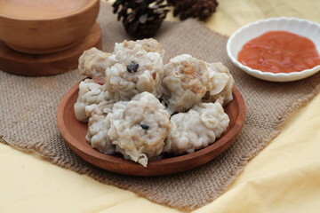 A plate of steamed dumplings served with a side of dipping sauce, placed on a burlap cloth with...