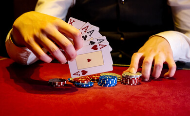 Player opens playing cards with one pair or two aces on red poker table. Close-up of playing chips...
