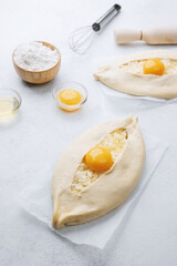 Uncooked khachapuri with egg yolk and whisk on white background