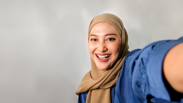 Young Asian woman in hijab surprised in blue t-shirt posing making video call while smiling isolated on white background.