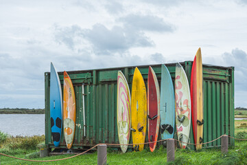 Row of colorful windsurfing boards leaning against a green container, Meldorf, Dithmarschen, Schleswig-Holstein, Germany