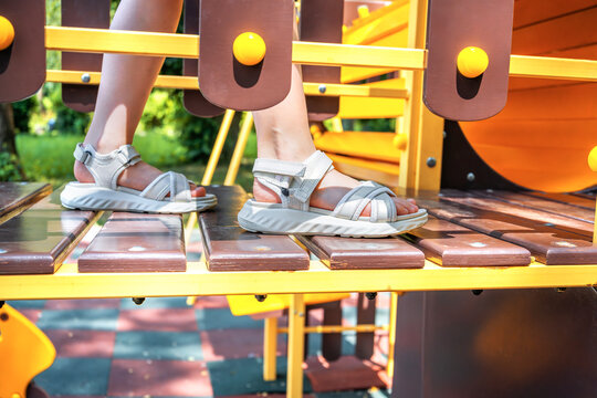 Close-up of a childs feet in sporty sandals walking on a wooden bridge at a colorful outdoor playground on a sunny day. - Powered by Adobe
