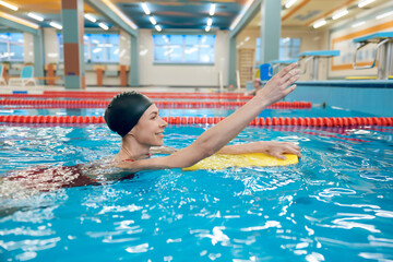 Cute caucasian young woman swimming in the pool with a board
