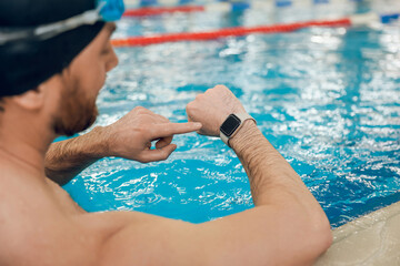 Man having a workout in the swimming pool and looking at his watch
