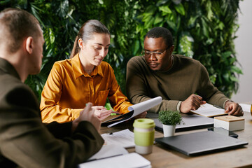 Young adult Caucasian woman discussing documents with young adult Caucasian man and young adult...