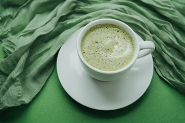 Macro shot of foamy matcha latte in white cup on green table
