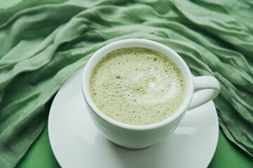 Cup of green matcha latte with soft textile on green background