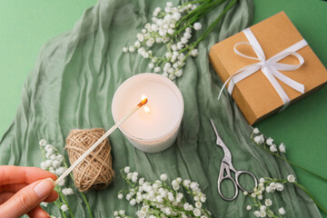 Hand lighting candle with flowers and gift on green background