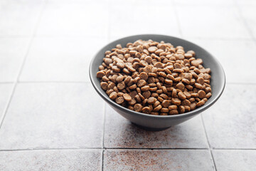 Bowl full of dry dog food kibbles on tiled background