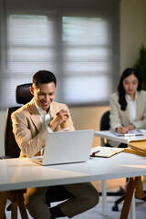 Fototapeta premium Smiling businessman enjoying coffee while working on laptop at office desk